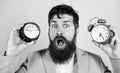 Man bearded hipster hold two different clocks. Guy unshaven puzzled face having problems with changing time. Time zone