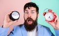 Man bearded hipster hold two different clocks. Guy unshaven puzzled face having problems with changing time. Time zone