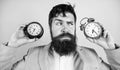 Man bearded hipster hold two different clocks. Guy unshaven puzzled face having problems with changing time. Changing