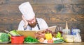 Man bearded hipster read book recipe near table fresh vegetables. Culinary arts. Recipe to cook healthy food Royalty Free Stock Photo