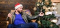 Man bearded hipster relax sit armchair near christmas tree. Man mature confident guy with beard relax at home. Warm and Royalty Free Stock Photo