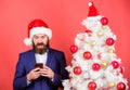 Man bearded hipster wear formal suit and santa hat hold smartphone. Send christmas greeting mobile message. Short