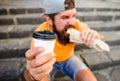 Man bearded shows paper cup drink stairs background. Take coffee with you. Fast food meal for lunch. Hipster bite hot