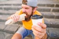 Man bearded shows paper cup drink stairs background. Take coffee with you. Fast food meal for lunch. Hipster bite hot