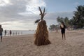 A man beats a tambourine near the Straw Scarecrow on a sandy beach by the ocean, during a ceremony for good weather and successful