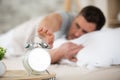 man in bed reaching to stop blank alarm clock