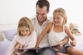 Man in bedroom with two young girls reading book Royalty Free Stock Photo