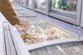 A man in a beige coat in the frozen food section of a large supermarket opens a refrigerator of vegetables. Close-up Royalty Free Stock Photo