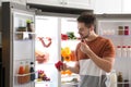 Man with bell pepper and grape berry near open refrigerator indoors