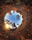 Man with bicycle on little planet with trees, soft blue sky and sunset. Mini planet of a park and sunset