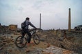 A man on a Bicycle looking down at the ruins of a zinc plant, destroyed brick buildings, the remains of the walls