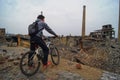 A man on a Bicycle looking down at the ruins of a zinc plant, destroyed brick buildings, the remains of the walls