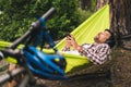 Man on bicycle trip at camping by lake is relaxing in green hammock while listening to music. Active recreation theme in Royalty Free Stock Photo