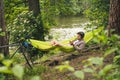 Man on bicycle trip at camping by lake is relaxing in green hammock while listening to music. Active recreation theme in Royalty Free Stock Photo