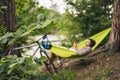 Man on bicycle trip at camping by lake is relaxing in green hammock while listening to music. Active recreation theme in Royalty Free Stock Photo