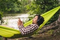 Man on bicycle trip at camping by lake is relaxing in green hammock while listening to music. Active recreation theme in Royalty Free Stock Photo