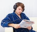 Man in big ear-phones on sofa reads newspaper Royalty Free Stock Photo
