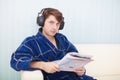 Man in big ear-phones on sofa reads newspaper Royalty Free Stock Photo