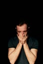 A man on a black background covers his face with his hands. The atmosphere of hopelessness,dejection Royalty Free Stock Photo