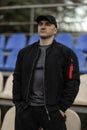 Man in black bomber jacket stands in empty stadium tribune with backpack during daytime Royalty Free Stock Photo