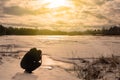 A man in black clothes photographs a landscape near a forest reservoir in early spring during sunset