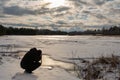 A man in black clothes photographs a landscape near a forest reservoir in early spring during sunset