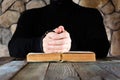 A man in black clothes with a rosary in his hands in front of an open old book the Bible or the Koran, the concept of prayer.