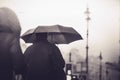 A man in black clothes and with a black umbrella, walking along a city street in rainy foggy dark weather, and a woman in a hood Royalty Free Stock Photo