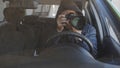 A man in black glasses and a hoodie at the wheel of a car is secretly shooting on a long-focus lens. Royalty Free Stock Photo