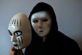 Man with black hood wearing a halloween white mask and holding a female mask Royalty Free Stock Photo