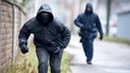 Man in black hooded sweatshirt and mask running on sidewalk Royalty Free Stock Photo