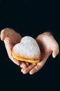 A man in a black hoodie holds a heart-shaped donut covered in powdered sugar. Royalty Free Stock Photo