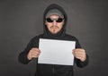 Man in the black hoody with hood wearing sunglasses holding empty sheet of paper