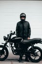 Man with a black motorcycle stands against a white garage door. Royalty Free Stock Photo