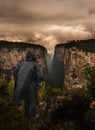 Man in black raincoat and hood standing on the edge of a cliff at sunset Royalty Free Stock Photo