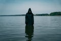 A man in a black robe with a hood stands in the river during the day. He mysteriously looks at the water Royalty Free Stock Photo