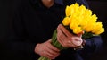 A man in a black shirt on a black background holds a bright bouquet of beautiful juicy yellow tulips to hand, give Royalty Free Stock Photo