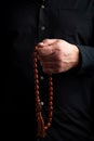 Man in a black shirt holds a brown stone rosary in his left hand, low key Royalty Free Stock Photo