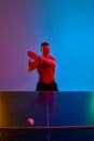 Man in black sport uniform playing table tennis, focused on ball to make perfect serve in neon light against gradient Royalty Free Stock Photo