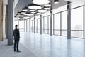 Man in black suit looking on city skyscrapers on background from business center high floor stylish hall with metallic pillars and Royalty Free Stock Photo