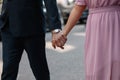 A man in the black suit and a woman in the pink dress are holding hands closeup. They are walking at the street Royalty Free Stock Photo