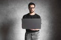 Man in a black T-shirt with a laptop on a gray background. Education, success, knowledge