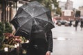 A man with a black wet umbrella was caught in a gust of wind on the street of the old city