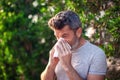 Man blowing nose in front of blooming tree. Spring allergy concept