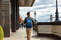 Man with blue bag on his back walking on riverside towards Tower Bridge in London