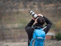 Man with a blue bag taking a photograph with a reflex camera and a zoom lens in the middle of the mountain