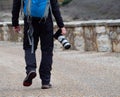 Man holding a camera with a big zoom objective outdoors in the middle of a path surrounded by a stone wall Royalty Free Stock Photo