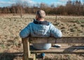 Man in a blue coat with the mobile phone sitting on the bench in a field