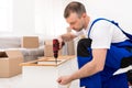 Man In Blue Coverall Assembling Wooden Shelf Using Drill Indoors Royalty Free Stock Photo