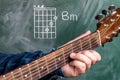 Man playing guitar chords displayed on a blackboard, Chord B minor